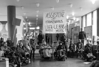Mehrere Menschen mit und ohne Rollstühle demonstrieren mit Transparenten für die Assistenz im Krankenhaus und bezeichnen diese als überlebenswichtig